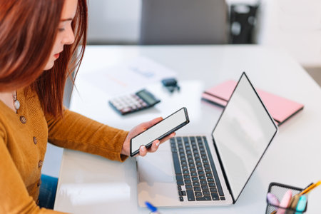 Young woman looking at her mobile phone and laptop.