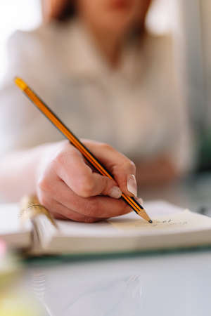 Young woman writing with pencil in notebook