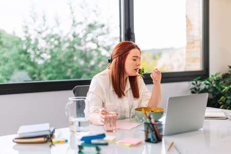 Healthy young woman eating salad while workingの写真素材