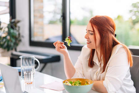 Healthy young woman eating salad while working