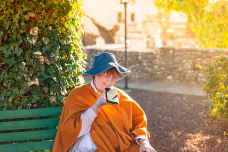 Old woman talking on a mobile phone on a bench in the garden. Spring sunset.の写真素材