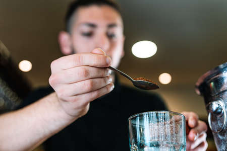 Young, modern waiter, adding brown sugar in a large crystal glass to prepare a mixer. Low angle viewの写真素材