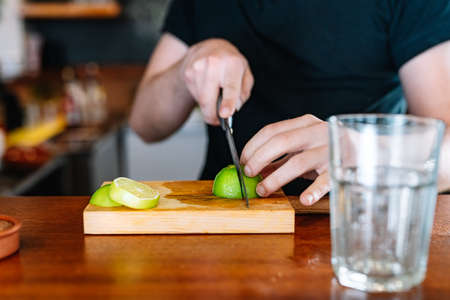detail of the hands of a young waiter cutting slices of citrus fruit to prepare a mixed drink.