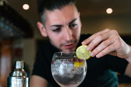 Young bartender garnishing with a slice of citrus fruit a cocktail in a crystal glass with ice.の写真素材