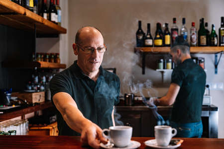 Two waiters at work, preparing coffee for their customers. Two co-workers in their small business.