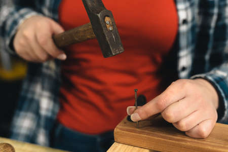 close-up of the hands of a young woman carpenter holding a nail in a wooden board.の写真素材
