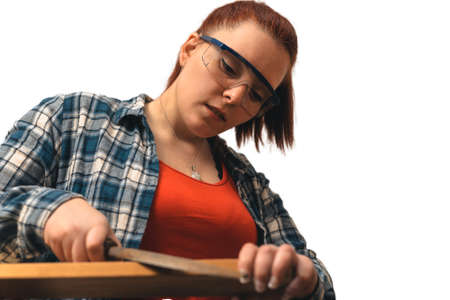close-up of a young woman, carpenter filing a wooden board with a file, in her small carpentry shop....