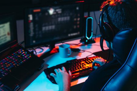 Young man addicted to video games playing on a computer with headphones. Young gamer illuminated...