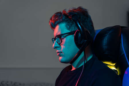 Young professional online video game player, playing on a computer. Young gamer illuminated with coloured lights.の写真素材