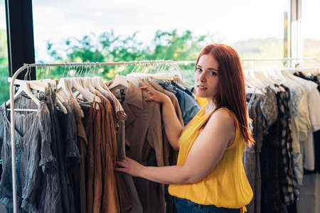 Young smiling and happy red-haired girl in a fashion shop. looking at camera. concept of shopping.