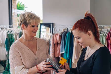 Clothes saleswomanas assistant advising a customer for a purchase. young woman paying for clothes with a credit card.の写真素材