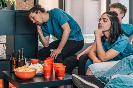 Football fans saddened by their teams defeat. Close-up of a table full of drinks and snacks for a...