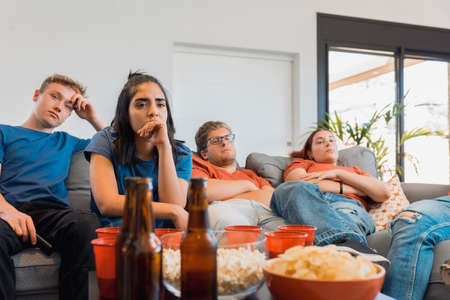 sad friends watching TV because their football team lost the game. upset young people at a house party.の写真素材