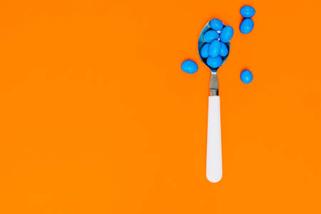 blue candies inside white spoon on orange background. assortment of candies. wallpaper to use text.の写真素材