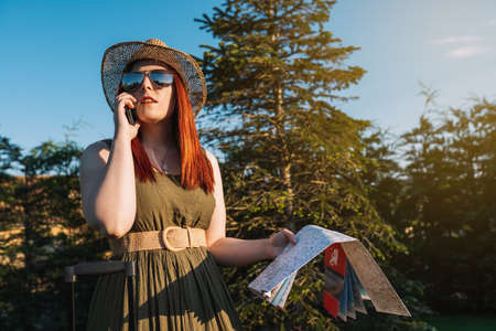 young red-haired girl calling with her smart phone for a taxi to pick her up at her resort. travel,...