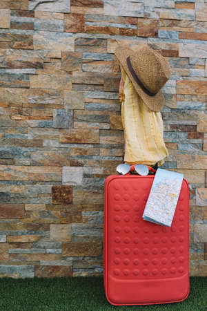 luggage in front of a stone wall and grass floor to use text. suitcase with hat, sunglasses, scarf and map.の写真素材