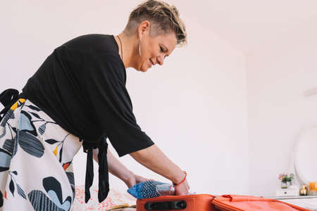 Blonde woman preparing luggage for her summer trip on the bed in the bedroom. Concept of leisure and holiday.の写真素材
