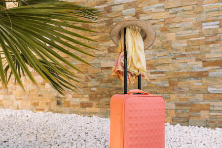 luggage in front of a stone wall and white stone floor, to use the text. orange suitcase with hat, sunglasses, sarong.の写真素材