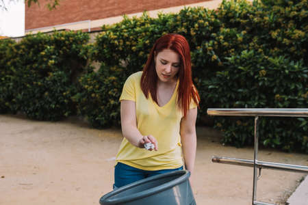 young woman recycling paper in a public waste bin in the city. responsible and environmentalist...