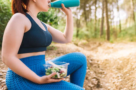 cropped shot of young sportswoman sitting drinking and eating healthy after sports training. girl...