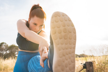 young sportswoman doing leg stretching exercises outdoors. female athlete training in nature. wellness and healthy living concept.の写真素材