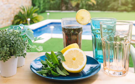 still life of glasses with mint and lemon soda, on a wooden table outside. Summer scene, drinks to...