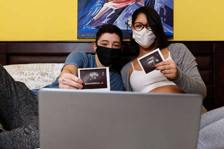 couple of future young parents showing ultrasound by laptop in an online video call, due to the...