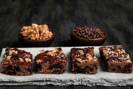 pieces of chocolate brownie and walnuts next to walnuts and chocolate in clay pots in the foreground, healthy food during quarantine at homeの写真素材
