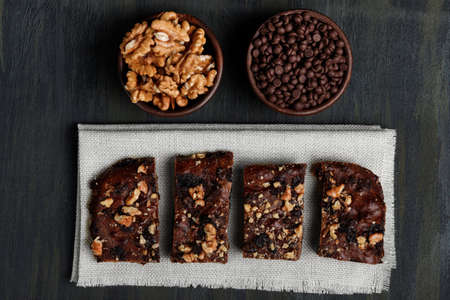 pieces of chocolate brownie and walnuts next to walnuts and chocolate in clay pots in the foreground, healthy food during quarantine at homeの写真素材
