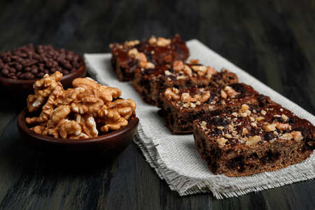 pieces of chocolate brownie and walnuts next to walnuts and chocolate in clay pots in the foreground, healthy food during quarantine at homeの写真素材