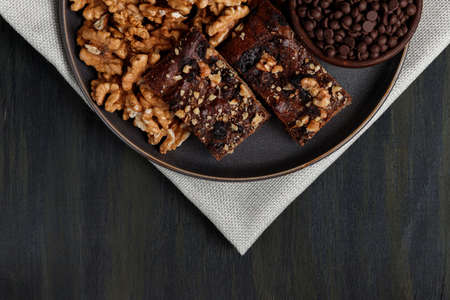 chocolate and walnut brownie next to walnuts and chocolate on a plate in the foreground, healthy food during quarantine at homeの写真素材