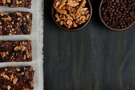 pieces of chocolate brownie and walnuts next to walnuts and chocolate in clay pots in the foreground, healthy food during quarantine at homeの写真素材
