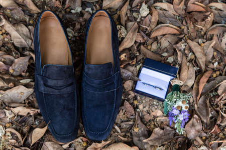 men's shoes and wedding rings on a background of dry leaves outdoorsの写真素材