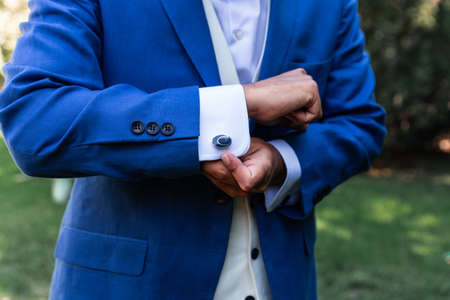 A groom in elegant suit buttoning cufflinks outdoors