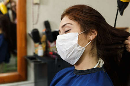 beautiful young woman with red hair at the hairdresser's during quarantine and social distancing as...