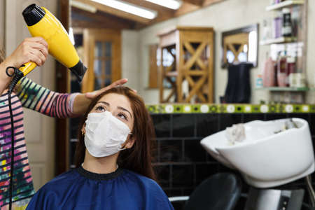 beautiful young woman with red hair at the hairdresser's during quarantine and social distancing as a result of covid-19の写真素材
