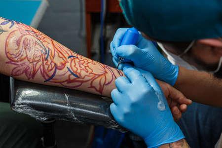 tattooist with his machine tattooing on the arm with the design drawn, concept of art and design