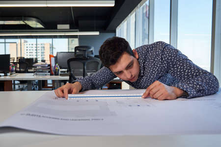 young and active entrepreneurial man architect and engineer, working in the office and measuring on...