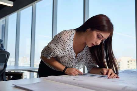 young, beautiful and empowered entrepreneurial woman architect, working in the office and measuring...