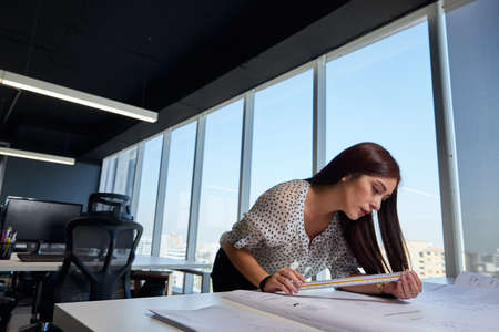 young, beautiful and empowered entrepreneurial woman architect, working in the office and measuring...