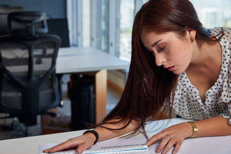 young, beautiful and empowered entrepreneurial woman architect, working in the office and measuring on her drawings and architectural plans, business concept, design and womanの写真素材