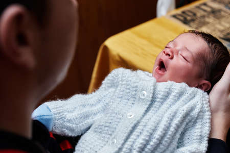 beautiful and adorable newborn baby held by his father in his hands while the baby sleeps and yawns,...