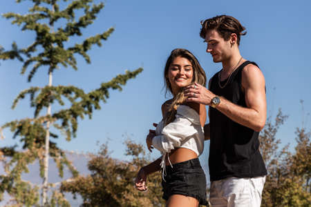young caucasian couple in love sitting down playing, laughing and sharing outdoors in nature, concept of love, park, back, fashionの写真素材