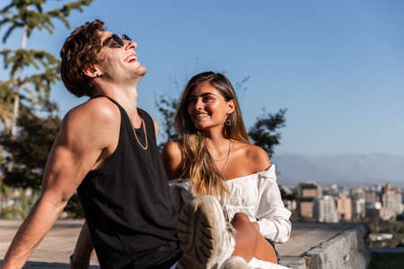 young caucasian couple in love sitting down playing, laughing and sharing outdoors in nature, concept of love, park, back, fashionの写真素材