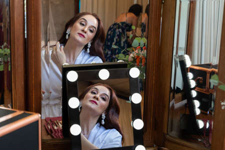 portrait of a beautiful redheaded Caucasian woman doing her makeup in front of the mirror for her...