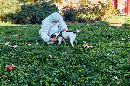young man with safety mask and surgical suit in the park with his chilean fox terrier dog petting...