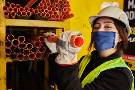 young woman wearing a mask, gloves and helmet in the middle of her work as a tool and building...