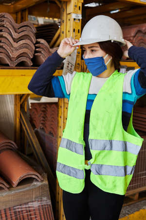 young woman wearing a mask and helmet preparing her work clothes as a saleswoman of tools and...