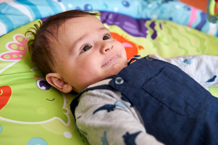 Newborn Caucasian baby lying on his back on a baby gym looking up and smiling, as seen from above,...