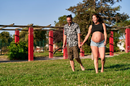 two young Latino future fathers walking hand in hand through the middle of the park while smiling and playing, pregnancy, love and new family conceptの写真素材